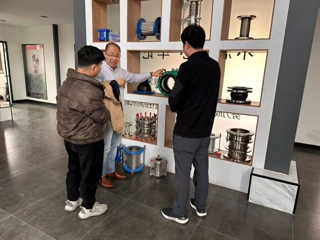 Customer product discussion in Hongze factory showroom showing expansion joints, metal hoses and pipeline connection products